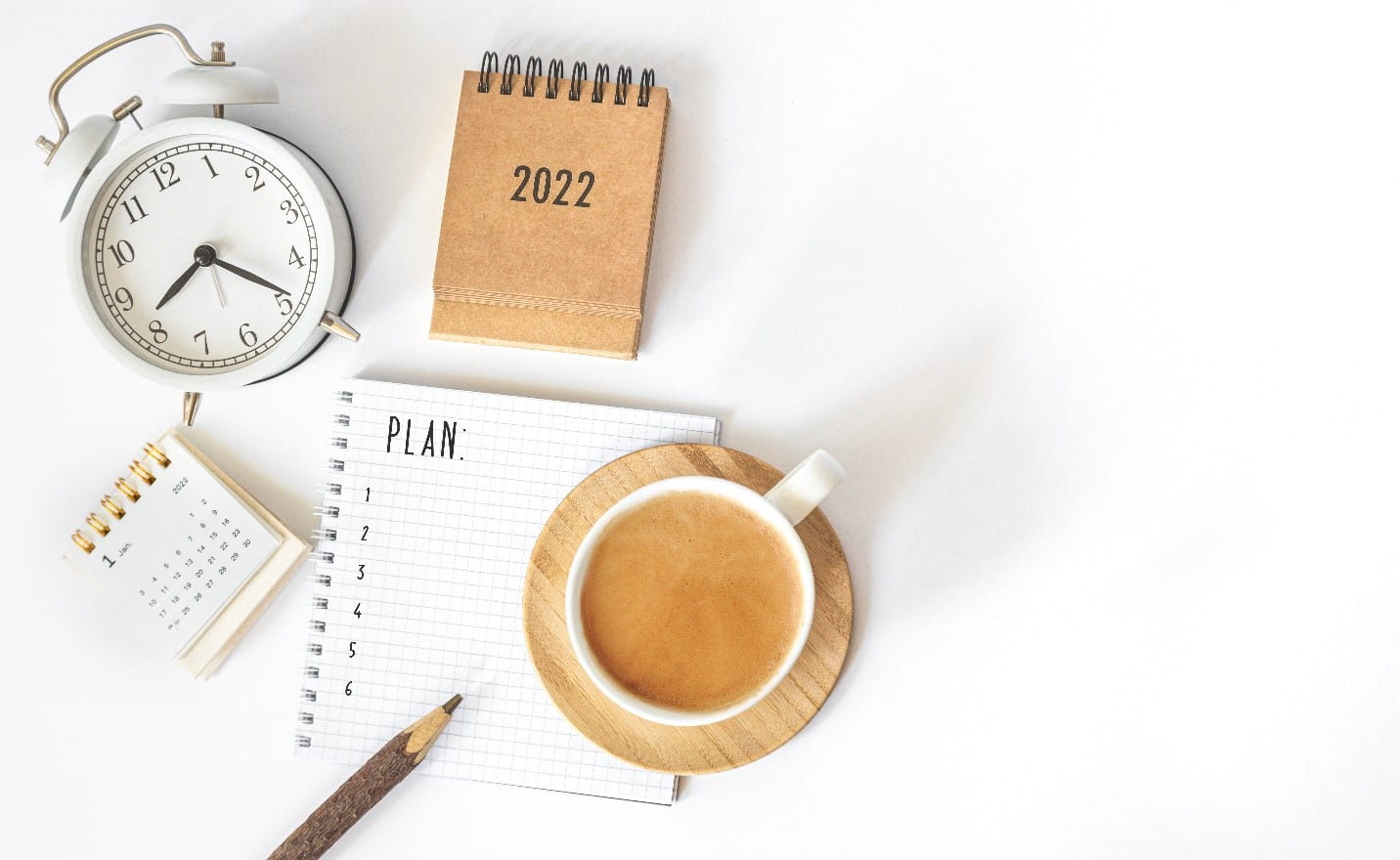 An image of a plan, calendar, cup of tea, clock and pencil on a desk.